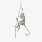 White resin monkey climbing a natural rope and holding a round bulb, on a plain white backdrop, shown as this Clérachic pendant light.