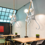 Two white monkey pendants on ropes with round bulbs, hung in a dining space with a white brick wall and pale wood tables, from Clérachic.