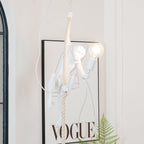 White resin monkey from Clérachic wrapped around a thick rope, its lit bulb glowing, with a framed print and a fern at the bottom of the frame.