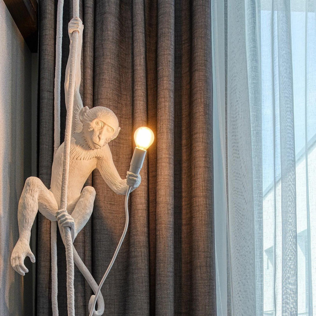 White monkey pendant lit in front of heavy brown curtains and sheer white drapes, its cord hanging in loops; from Clérachic.