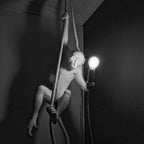 Black-and-white photograph of the monkey pendant on its rope, holding a lit bulb against a dark corner; this Clérachic design in monochrome.
