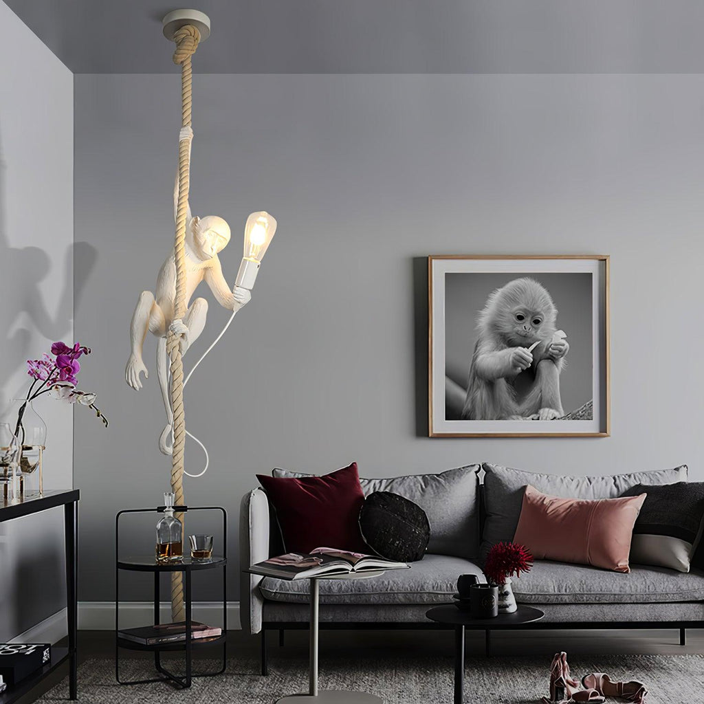 This Clérachic pendant hangs from a ceiling canopy above a grey sofa in a living room, the white monkey lit, with a framed monkey portrait on the wall.