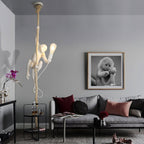 This Clérachic pendant hangs from a ceiling canopy above a grey sofa in a living room, the white monkey lit, with a framed monkey portrait on the wall.