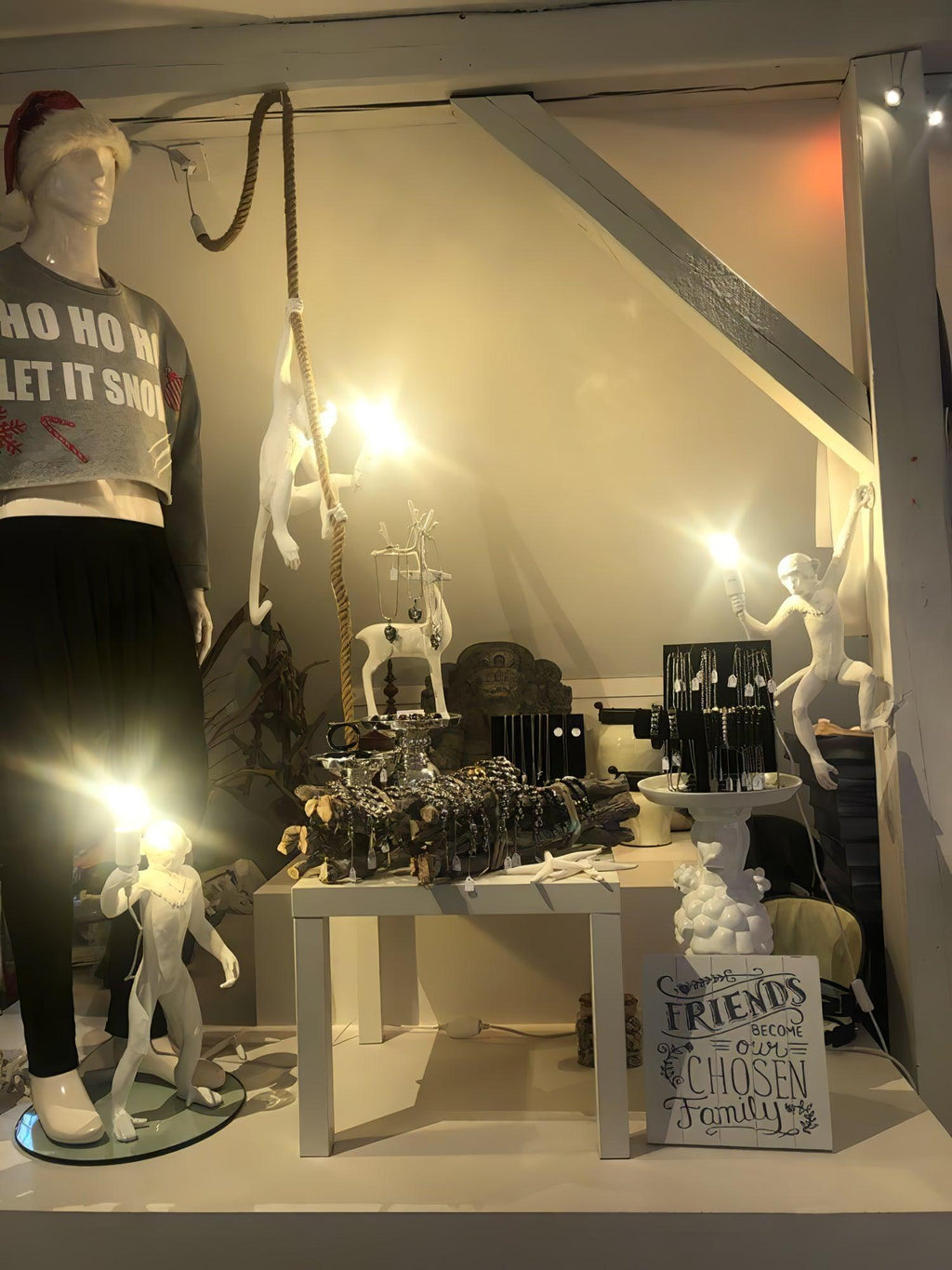 Shop display with several white monkey lights, one hanging, one standing and one on a table, lit among accessories in an attic space; Clérachic.