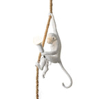 White resin monkey gripping a thick natural rope with a round frosted bulb in hand, on a white background; this Clérachic pendant light.