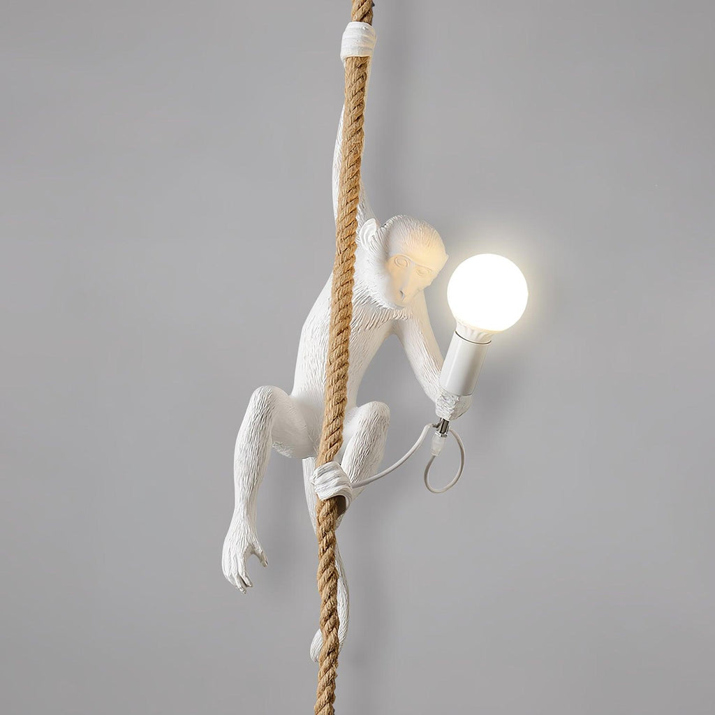 Side view of the white monkey on its rope with a frosted round bulb glowing, and its cord looped beneath, on a grey wall; from Clérachic.