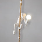 Side view of the white monkey on its rope with a frosted round bulb glowing, and its cord looped beneath, on a grey wall; from Clérachic.