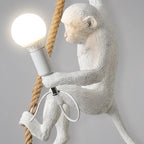 Close view of the monkey's face, shoulder and the bulb holder on this Clérachic pendant, with the thick rope and cord loop beside it.