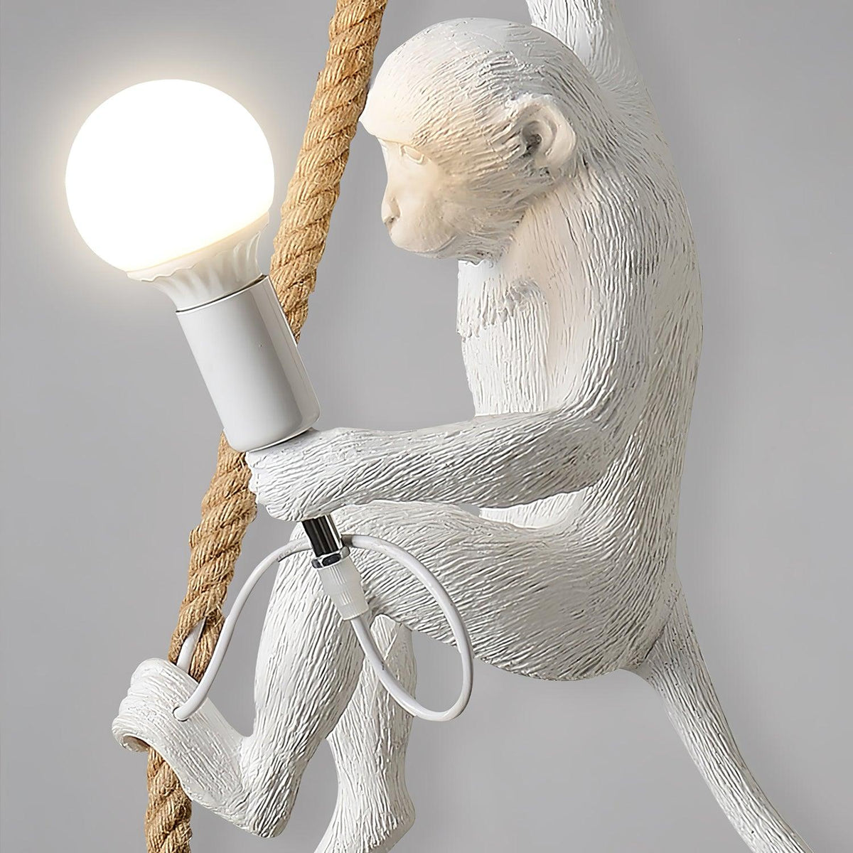Close view of the monkey's face, shoulder and the bulb holder on this Clérachic pendant, with the thick rope and cord loop beside it.
