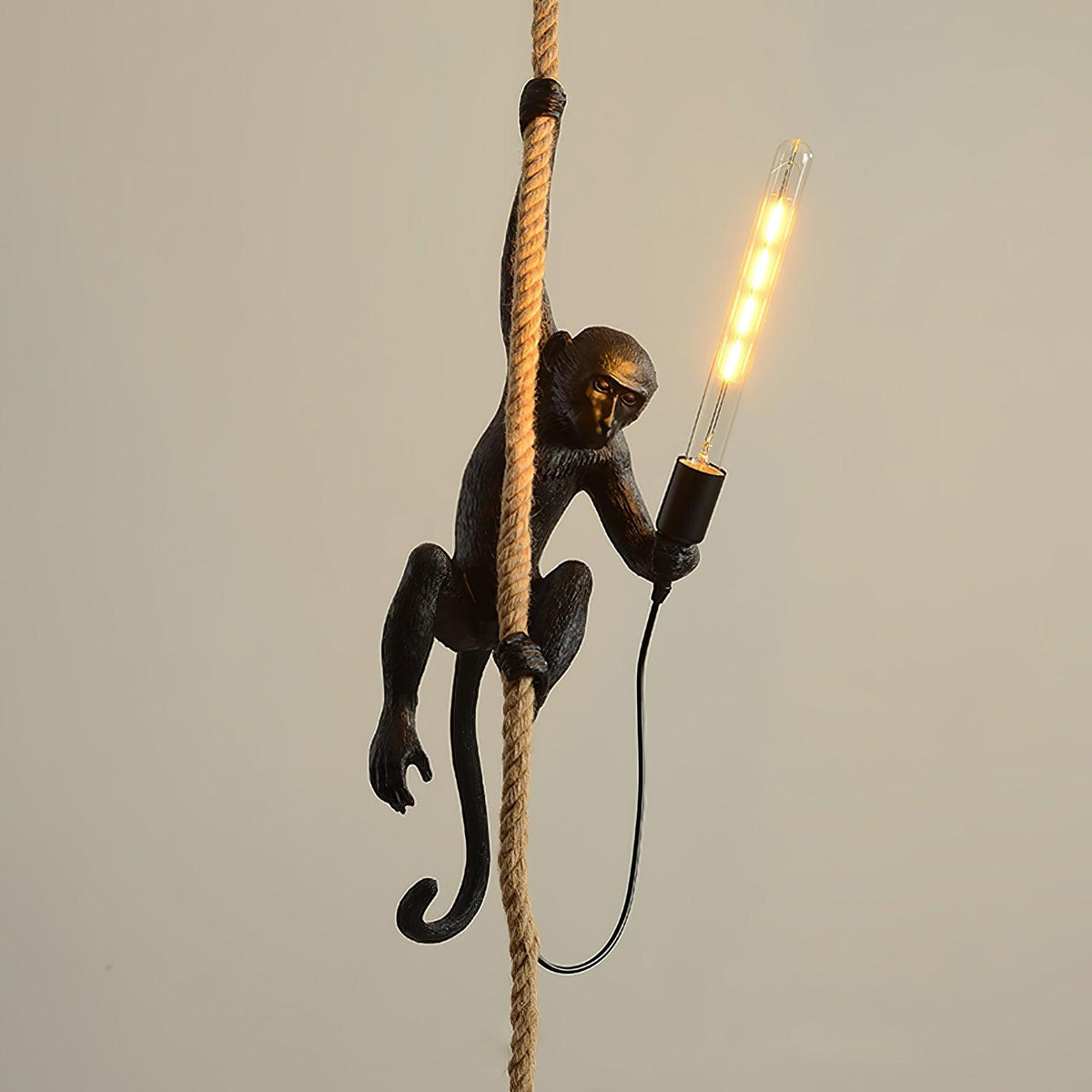 Black monkey on a thick rope holding a long glowing filament bulb, against a plain beige wall, as a Clérachic pendant.