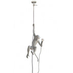 Full-length view of a white monkey pendant from its round ceiling canopy down a thin rope to the figure and its bulb; from Clérachic.