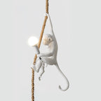 White monkey with a round bulb lit in its hand, climbing a natural rope against a soft grey background; this Clérachic pendant.