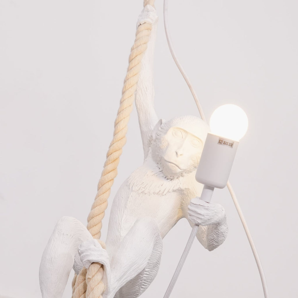 Close view of the white monkey's face and arm, a lit round bulb in its grip and a thick twisted rope beside it; this Clérachic pendant.