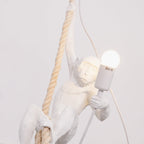 Close view of the white monkey's face and arm, a lit round bulb in its grip and a thick twisted rope beside it; this Clérachic pendant.