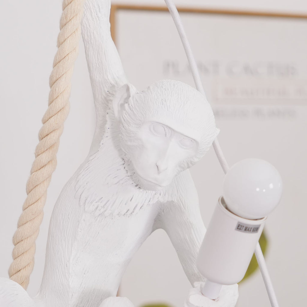 Detail of the monkey's face, textured fur and the white bulb holder it grips on this Clérachic pendant, with the rope running behind.