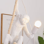 White monkey leaning on its thick rope with a glowing bulb in hand, a framed botanical print behind; a nearer view of this Clérachic pendant.