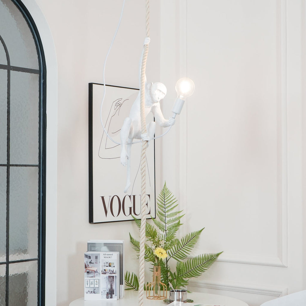 White monkey with a glowing bulb hanging above a table with a fern and magazines, in front of an arched window; from Clérachic.