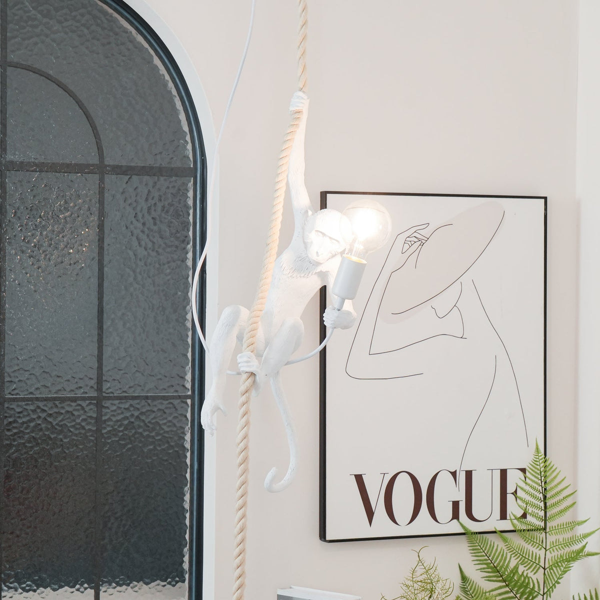 White monkey and its glowing round bulb in front of an arched window and a large framed print, with a fern at the bottom; from Clérachic.