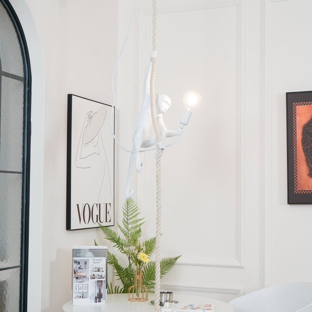 This Clérachic pendant hangs with its white monkey lit beside a leopard print, with a framed print, a fern and books below.