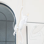 White monkey holding a clear filament bulb, with a thick rope above it and an arched window behind; a nearer view of this Clérachic pendant.