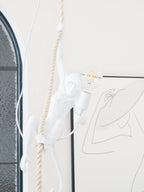 Narrow view of the white monkey gripping the rope with a filament bulb lit, in front of an arched window; from Clérachic.