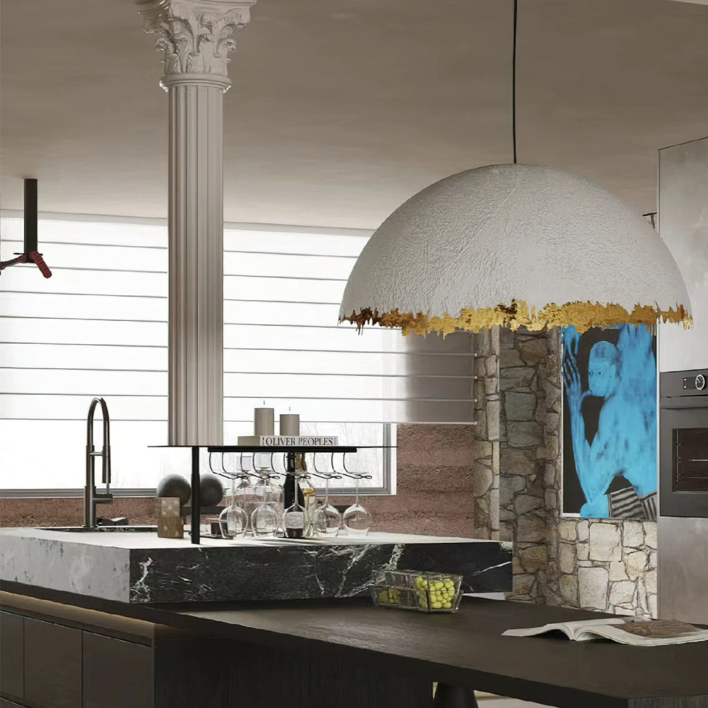 Large Clérachic dome pendant with a jagged gold rim hangs over a dark stone kitchen island, with a fluted white column behind.