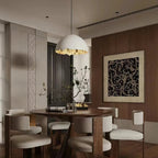 A Clérachic dome pendant with a gold rim hangs above a round dark wood table and cream chairs in a wood-panelled room.
