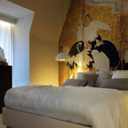 A small Clérachic dome pendant glows by a bed with a white fur throw and a gold-leaf screen painted with cranes.