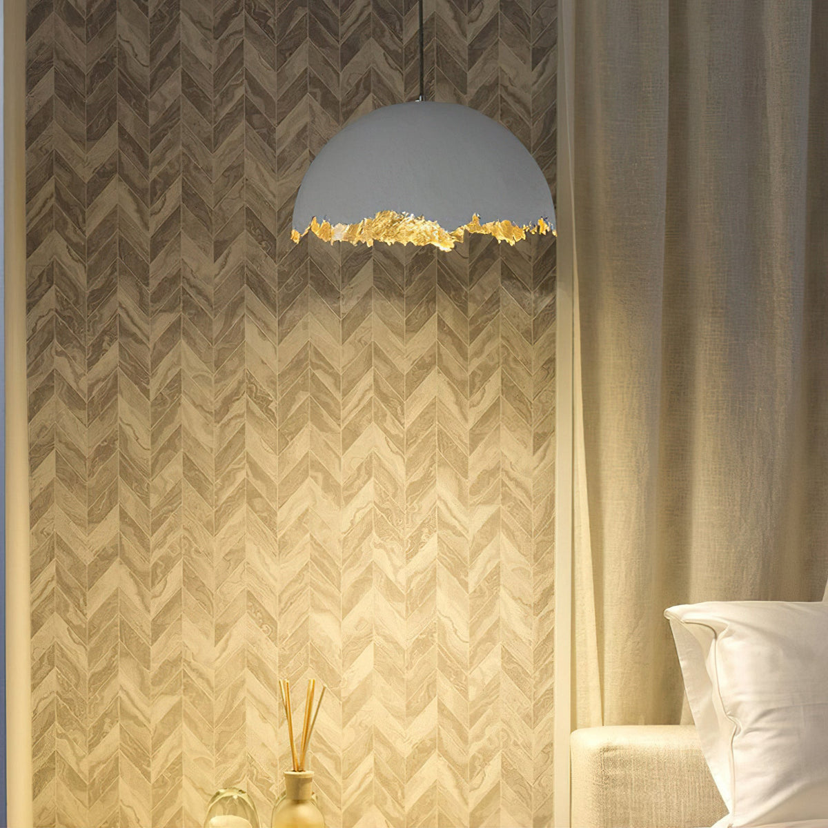 Clérachic dome pendant with a jagged gold edge lit warm, against a chevron wall with a curtain and a pillow below.