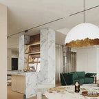 Clérachic dome pendant with a ragged gold rim hangs in a marble-clad open-plan room with a green sofa in the distance.
