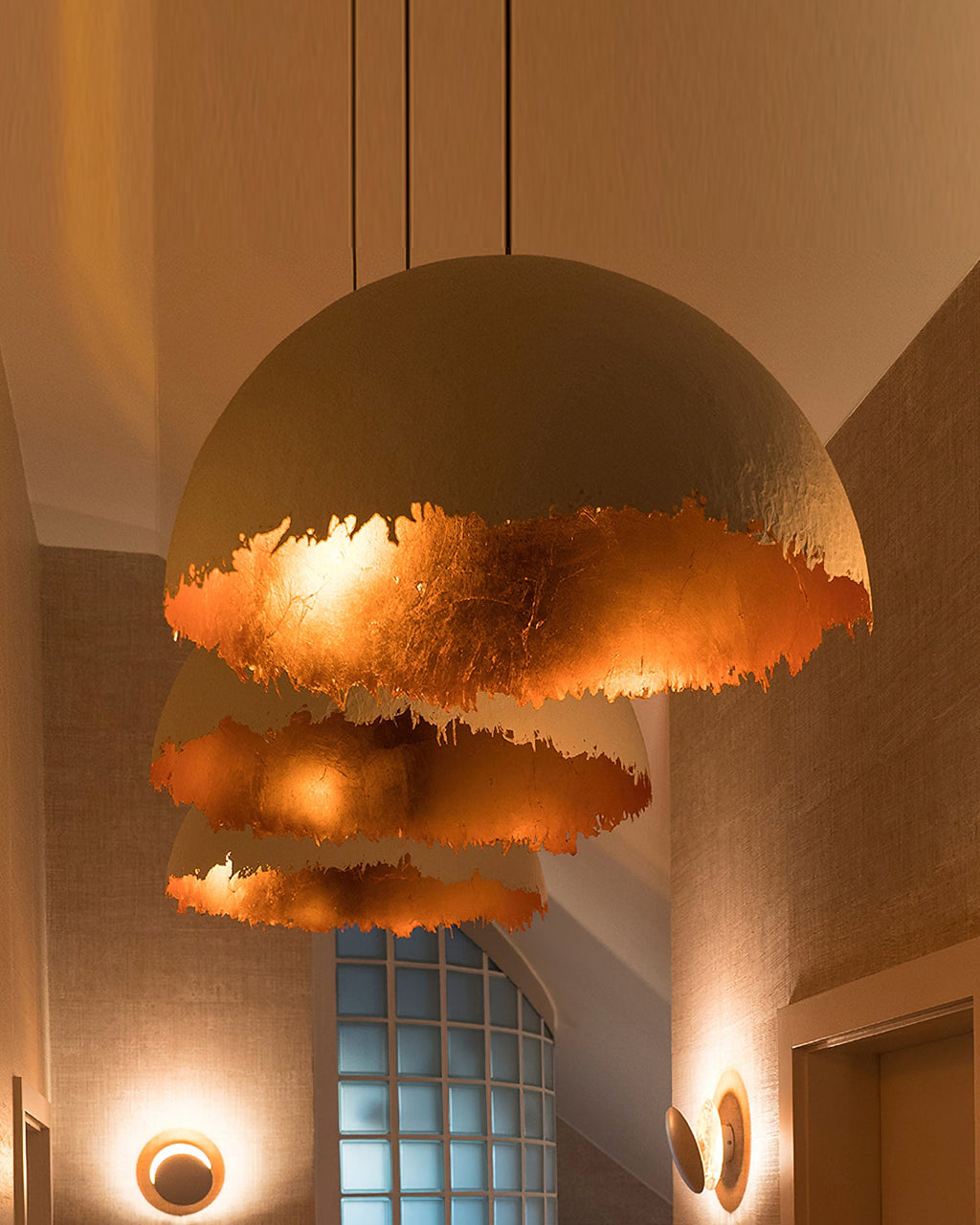 Three Clérachic dome pendants hang one below the other, glowing orange-copper inside, over a stairwell with glass blocks.