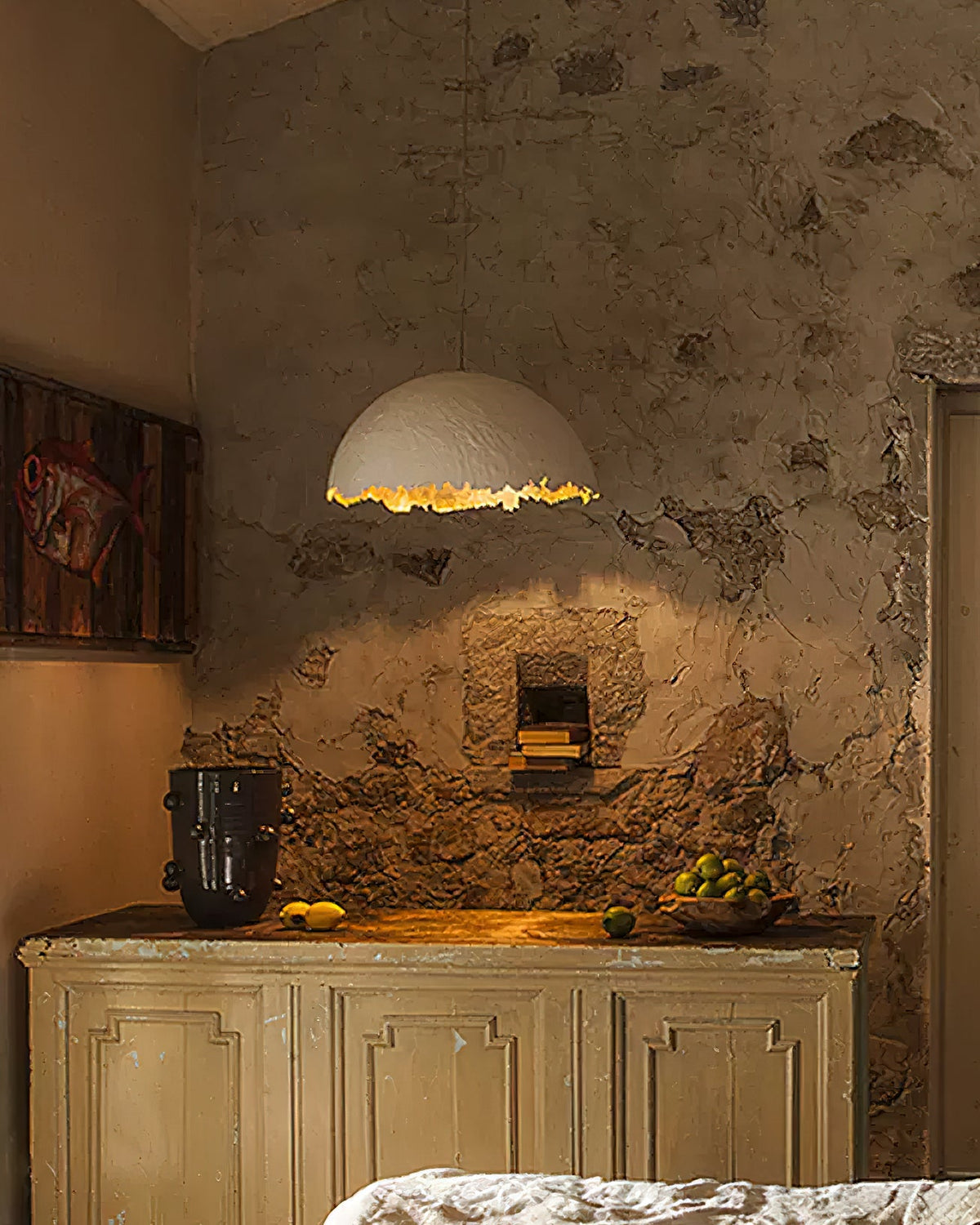 A Clérachic dome pendant with a gold rim hangs above a worn plaster wall and a cream cabinet, lit warm.