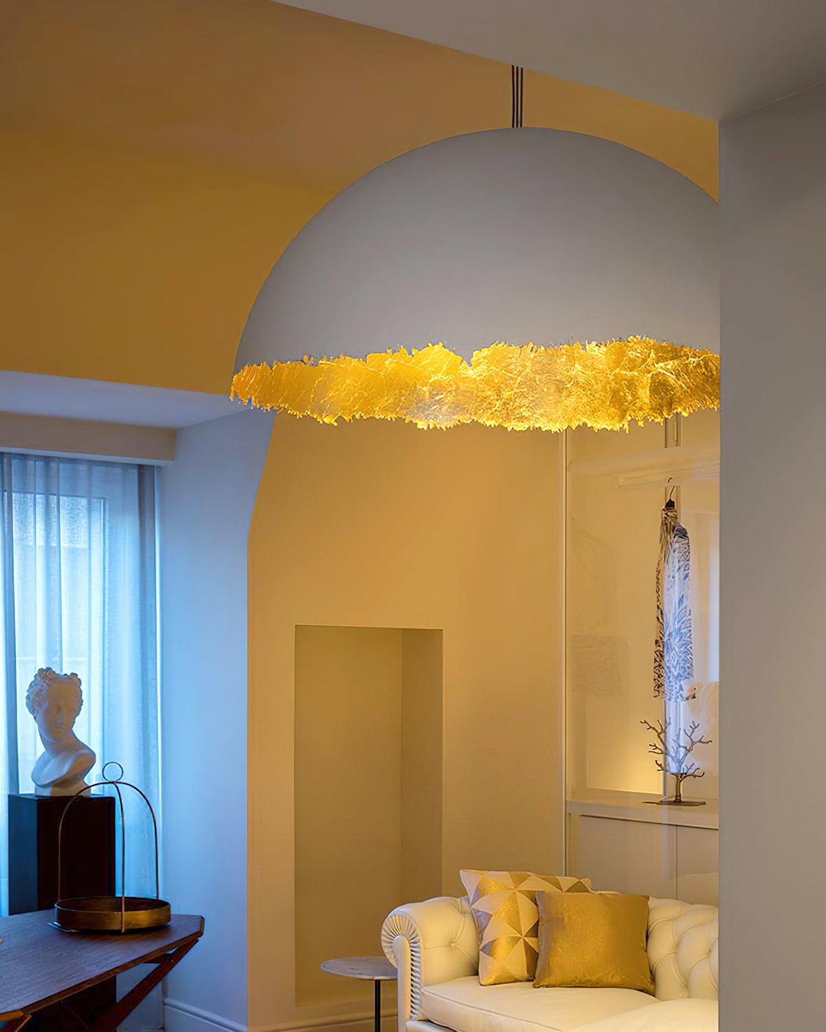 A large Clérachic dome pendant with a gold-leaf rim hangs in a yellow room with an alcove and a cream sofa.