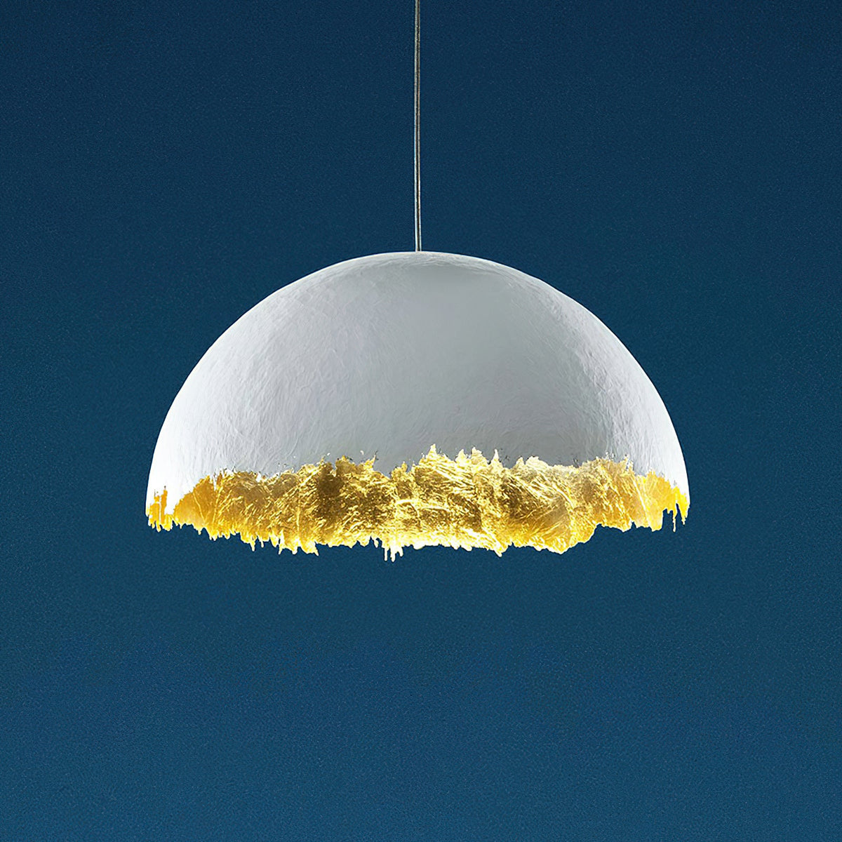 Clérachic dome pendant in white with a jagged gold-leaf lower edge, shown on a deep blue studio backdrop.