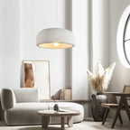 A Clérachic dome pendant hangs in a pale living room above a curved grey sofa, a round coffee table and a vase of dried pampas grass.