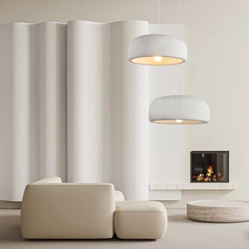 Two Clérachic dome pendants at different heights in front of a curved white wall, above a beige sofa and a lit fireplace.