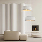 Two Clérachic dome pendants at different heights in front of a curved white wall, above a beige sofa and a lit fireplace.