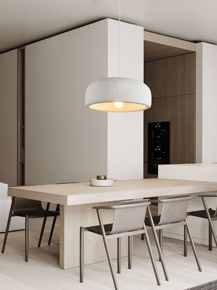 A Clérachic dome pendant lit warm above a pale wooden dining table with slim chairs, in front of a white column and dark wood cabinets.