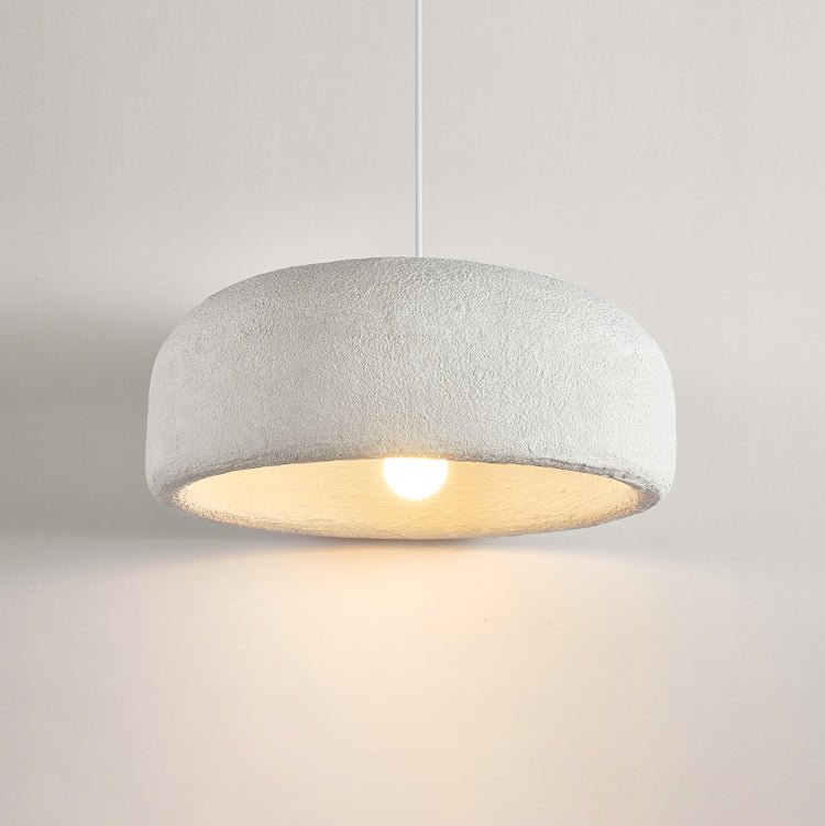Close view of the textured white shade of this Clérachic pendant, with the bulb glowing and warm light on the wall below.