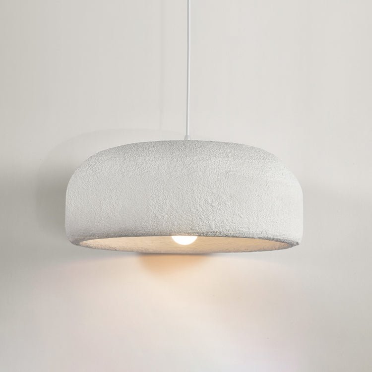 A Clérachic dome pendant hung against a pale wall, its rough white shade and bulb casting a soft pool of warm light.