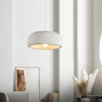 A Clérachic pendant lit above a corner with a framed print, a vase of dried grasses and curved white walls.
