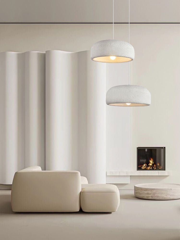 Two Clérachic dome pendants at different heights hang near a curved white wall, with a beige sofa and a lit fireplace below.