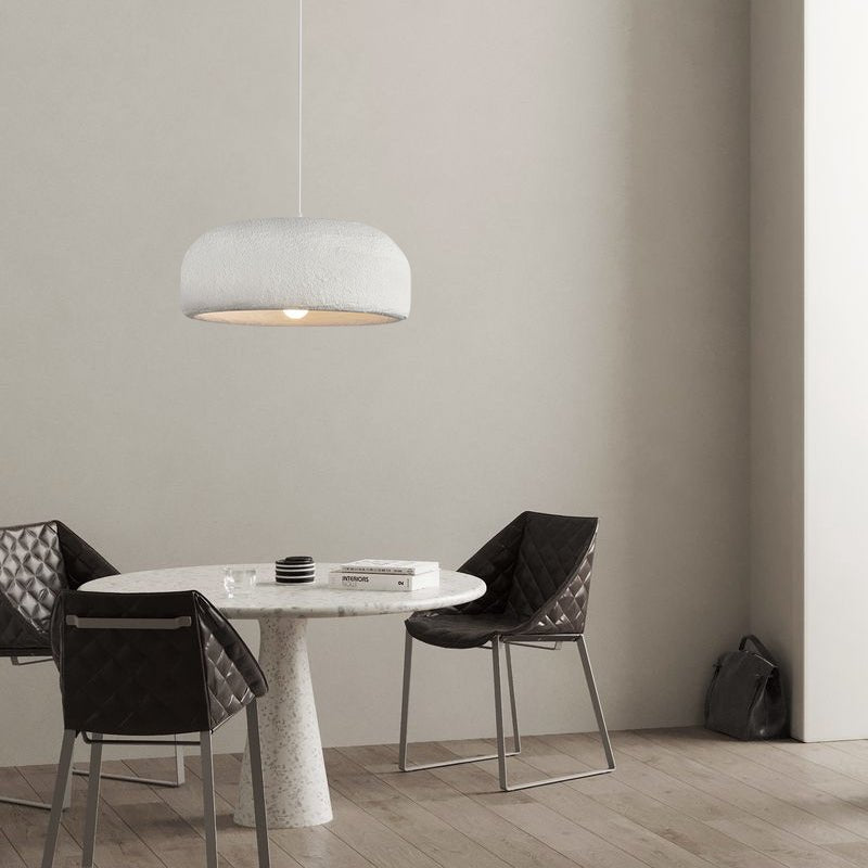 A Clérachic dome pendant hangs above a small round marble-topped table with two dark quilted chairs, in a grey-beige room.