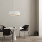 A Clérachic dome pendant hangs above a small round marble-topped table with two dark quilted chairs, in a grey-beige room.