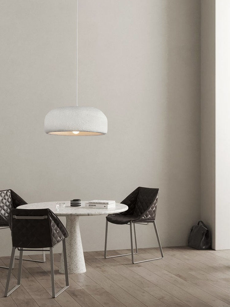 A smaller view of this Clérachic pendant above the round table and dark chairs, with a bag on the floor by the wall.