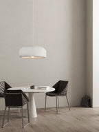 A smaller view of this Clérachic pendant above the round table and dark chairs, with a bag on the floor by the wall.
