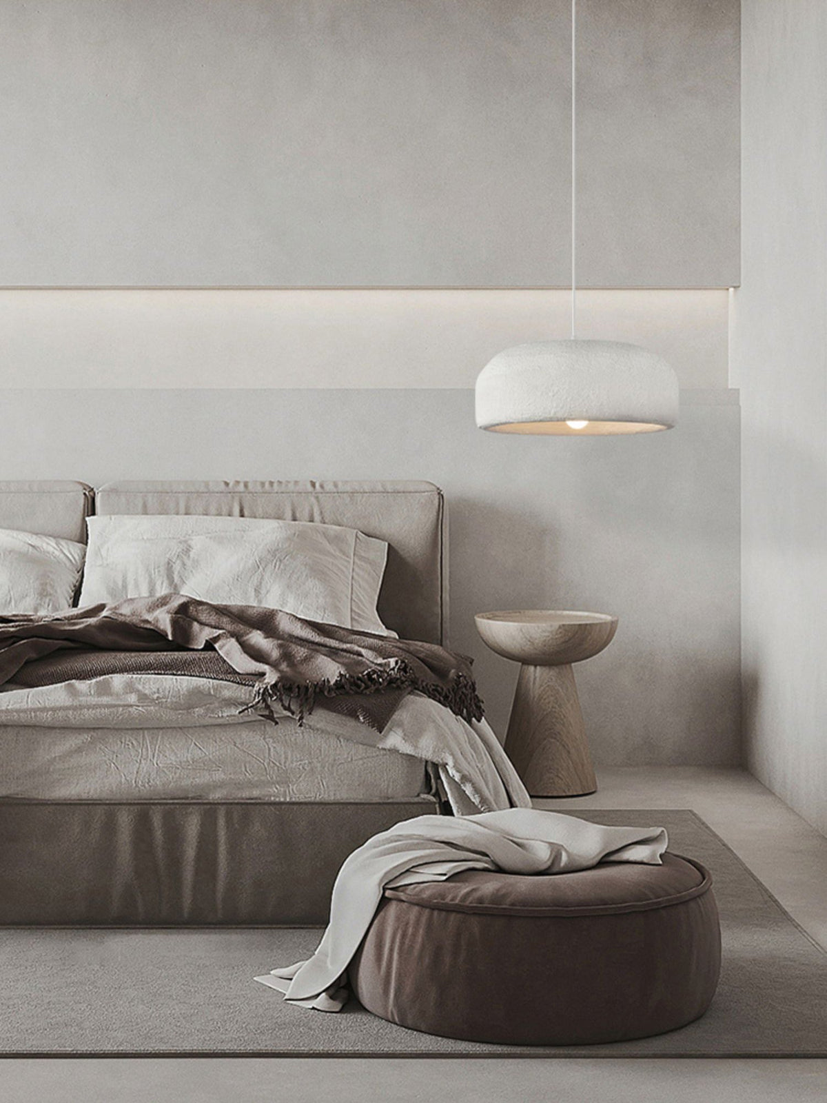 A Clérachic dome pendant hangs above a neutral bedroom with a grey bed, a rumpled throw and a round brown pouffe.