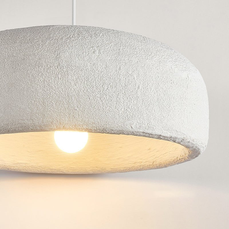 Close view of the rough plaster-like texture on this Clérachic pendant shade, with the bulb glowing warm beneath it.