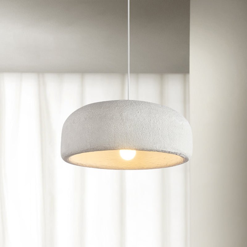 A Clérachic dome pendant hangs in front of sheer white curtains, its textured shade lit warm from the bulb below.