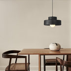 This black Clérachic pendant hangs high in the corner of a dining room above a walnut table with a pale stone bowl and cane-seated chairs.